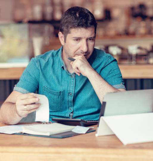Café owner reviewing bills and finances on a laptop, showing the financial stress many small businesses face.